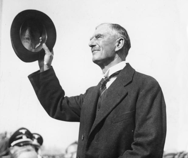 Neville Chamberlain, waving his hat to the crowds, arrives at Munich