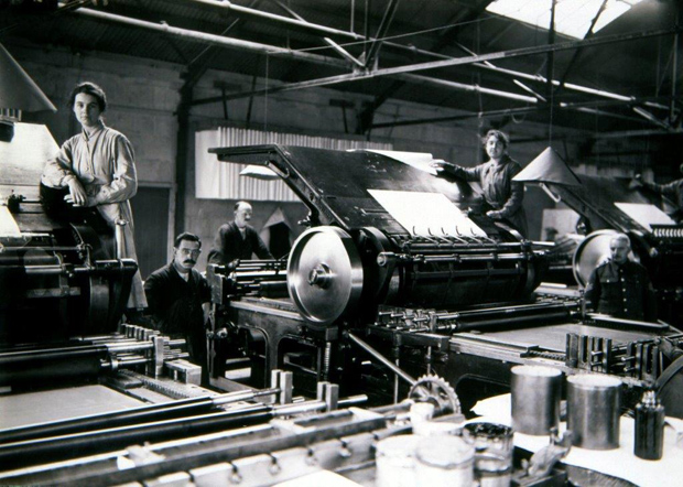 A printing press factory, with several workers in overalls posed formally for the photograph - the size of the printing press machines is impressive.