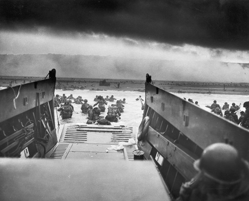 Allied troops wading through water and jumping off the boat onto the Normandy shore