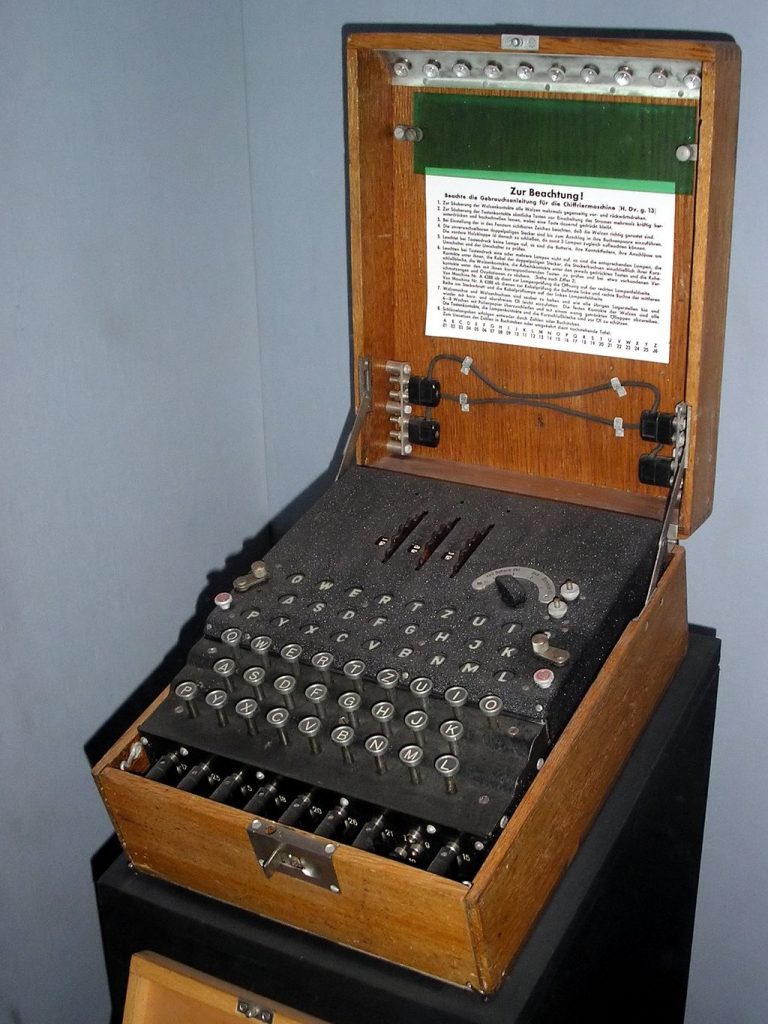 An old fashioned looking device - in the wooden box, there are old fashioned typewriter keys and electricals. The lid has some German writing on it.